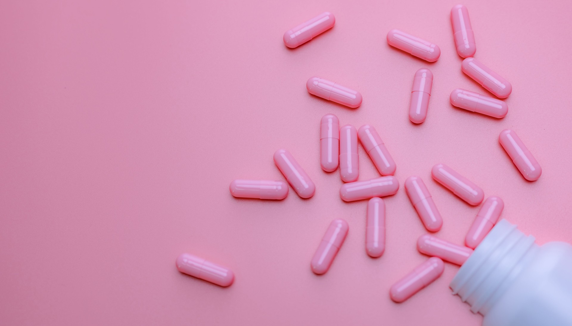 Píldoras de cápsulas rosadas extendidas fuera de la botella de plástico de la droga. Concepto de seguro de salud de la mujer y cáncer de mama. Vitaminas y suplementos para una piel sana. Banner web de farmacia. Antecedentes de farmacia en línea.